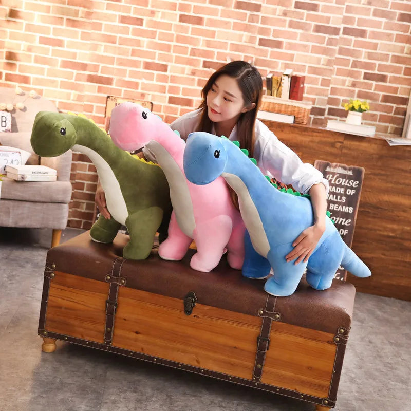 Woman holding three colorful dinosaur plush toys on a wooden chest in a room with a brick wall.